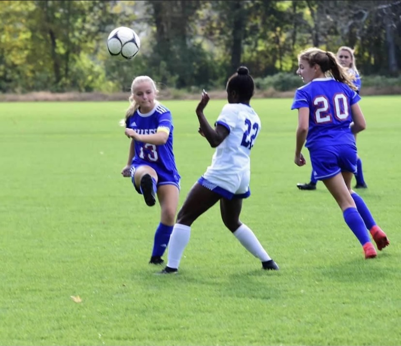 Mia Higgins (#13) kicking the ball past the defender with Mallory Tomkalski (#20) and Reilly Faraci (in the back) playing defense