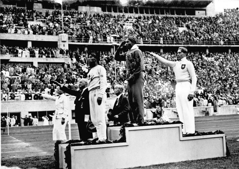Jesse Owens, center, salutes the American flag during a medal ceremony at the 1936 Summer Olympics in Berlin, Germany, alongside a German competitor delivering a Nazi salute. Topics such as civil rights, politics, and nationalism will be covered in the new Sports and Society class, which begins in the fall.