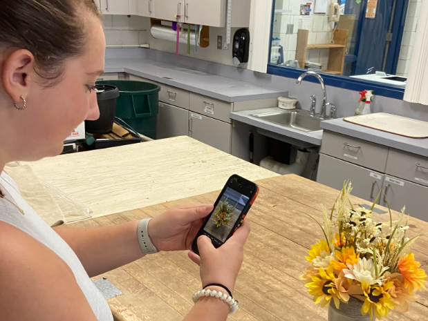 Junior Alexa Sweeney takes a photo of her floral arrangement in her floriculture class Sept. 22. Teachers like Eric Birkenberger allow their students to use their phones during class time to take photos of their projects. 
