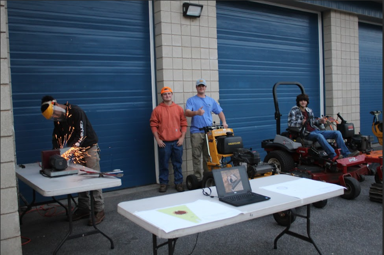 Junior, Cameron Frasier, demonstrates the process of sharpening blades in landscaping class.  Current landscaping students display the array of equipment to give the 8th graders a look of what they use in class. “My main goal was to convince [8th graders] to come here, and show them how cool the program is.” Frasier ( pictured left), said. 