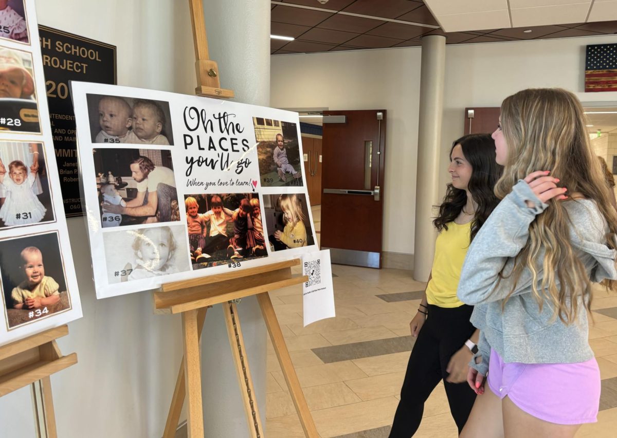 Students Hailey Goldman, left, and Aubrie Salisbury look at Nonnewaug staff baby pictures, which are posted out in the main lobby for Teacher Appreciation Week, which is sponsored by the Future Educators Club.