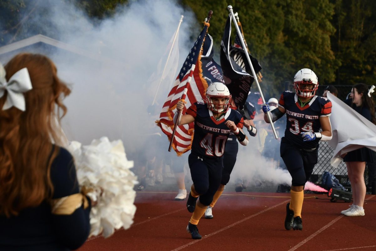 Chase Heidorn (40) and Tristan Vandyke (34) runs with the flags to open the Northwest United football homecoming game vs. Thames River on Sept. 19.