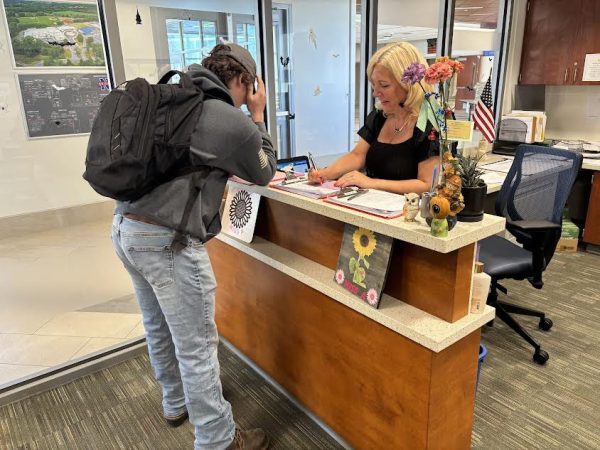 Dylan Loring, left, signs into school late and gets a tardy pass and lunch detention slip from secretary Jennifer Alena.