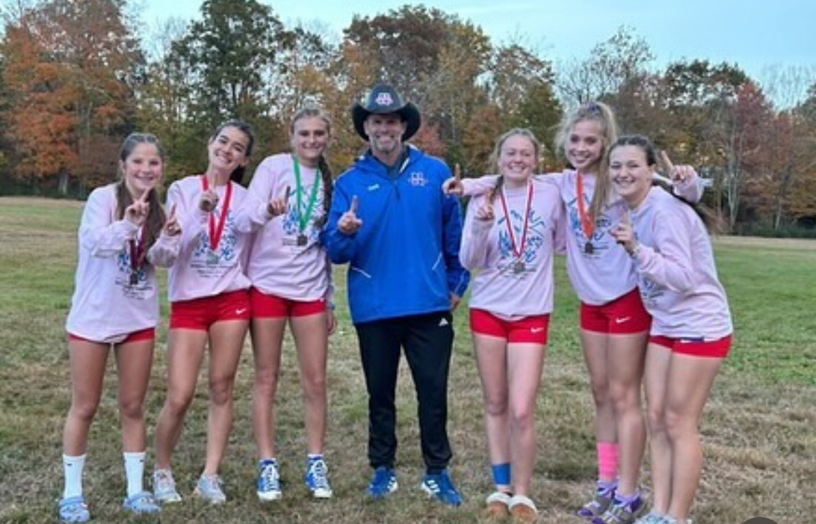 The Nonnewaug girls cross country team, from left, Thea Oleynikov, Madeline Garguilo, Scarlett Ivey, coach Arleigh Duff, Mackenzie Scully, Grace Rubacha, and Flora Frangu, pose with their first-place medals at the Berkshire League championships. (Courtesy of Nonnewaug cross country/Instagram)

