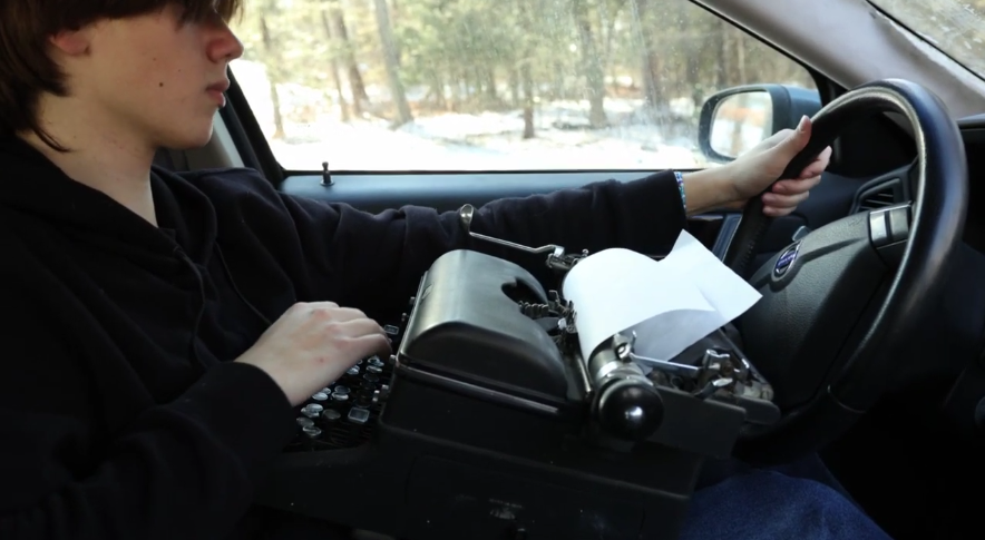 Voros holds a typewriter while driving in a frame of the winning video. The pair utilized a typewriter to emphasize how just because typing is easier now, does not mean it is safer on the road. (Photo Credit: Smith and Voros) 