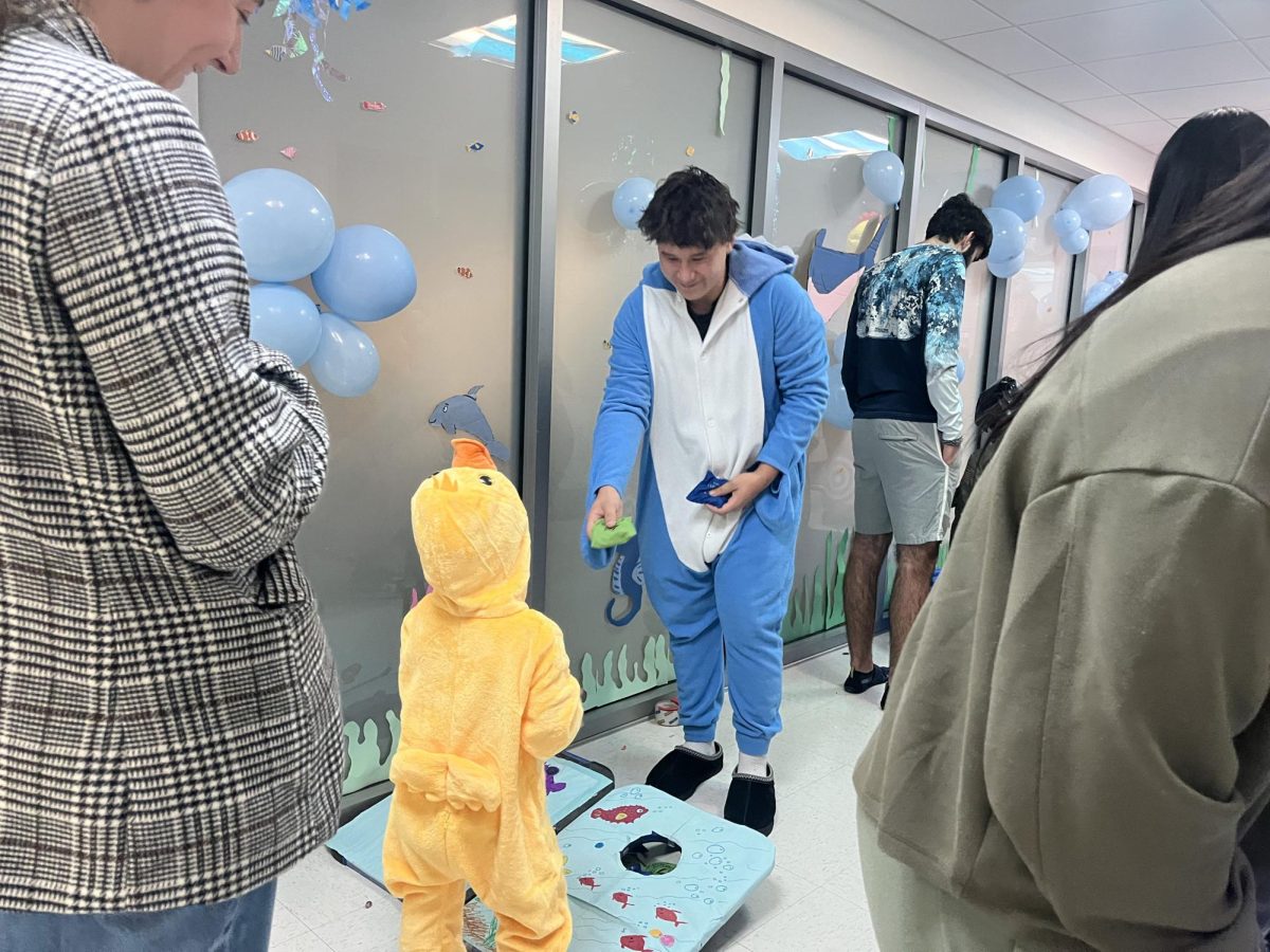 Senior Jonathan Cheung hands a bean bag to a little kid to participate in the bean bag toss at Trick or Treat Street. Cheung worked at both in both the National Math Honor Society and the Science National Honor Society. (Photo Contributed)