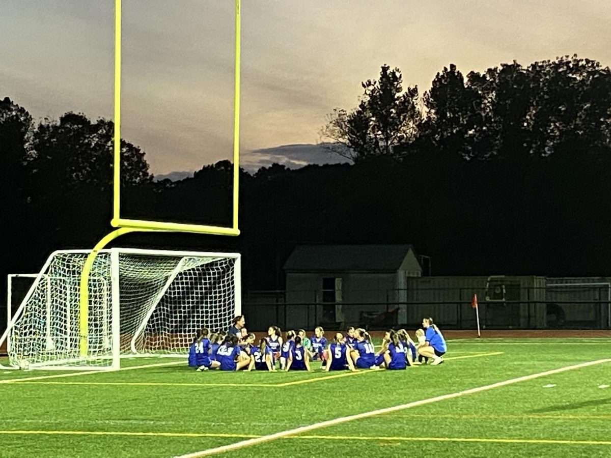 The girls varsity soccer team has a meeting during half time under the lights of the turf field.
