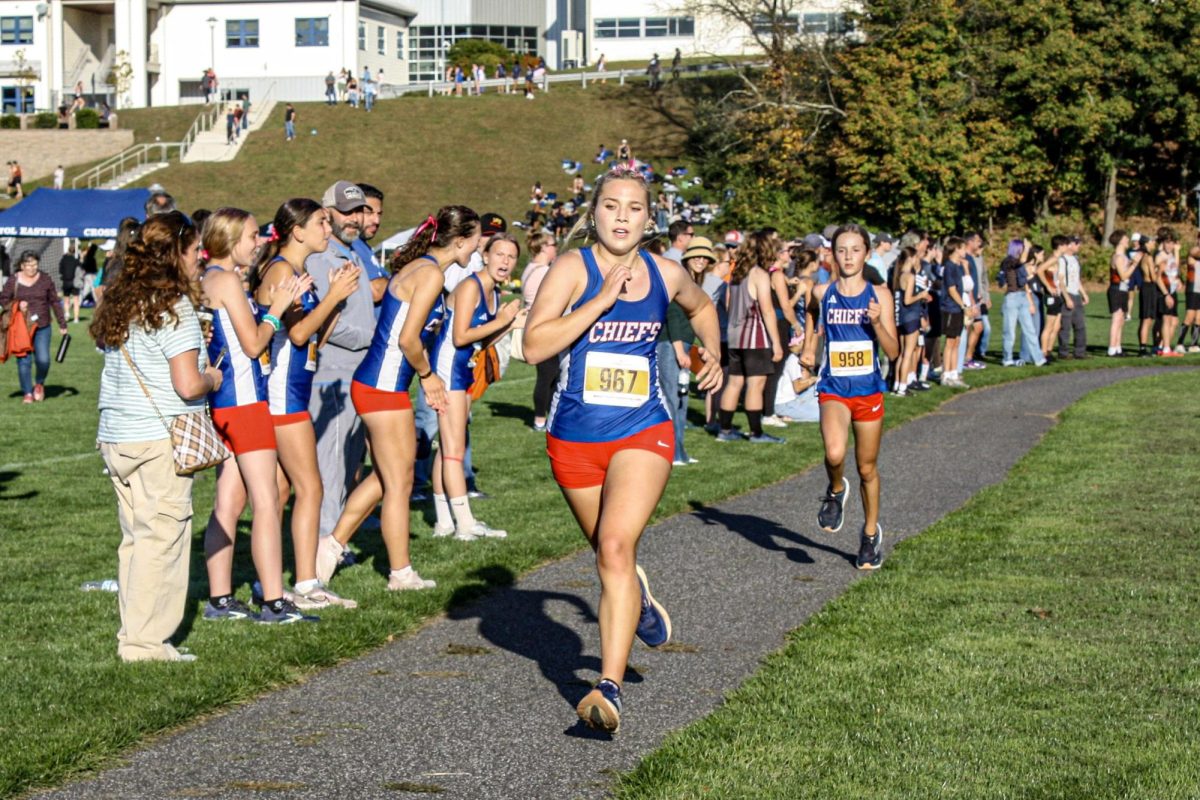 Grace Rubacha followed by Valerie Chandler race to the finish line with fellow Chiefs cheering them on at the Nonnewaug Cross Country Invitational Oct. 3.