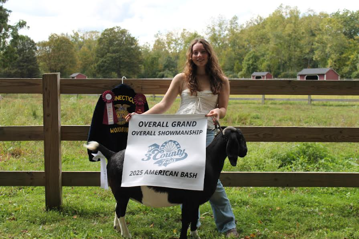 Christa Freel holding her awards from goat shows; awards being- winning Grand Champion Showman, 1st,2nd, & 3rd place ribbons, and the goat that got her there Tulsi.  