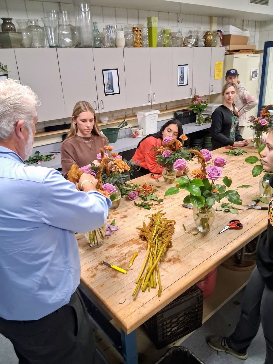 The class meets in the head house to wrap things up with the arrangement. Eric Birkenberger explains how to proceed with the rest of the flowers, specifically the roses.