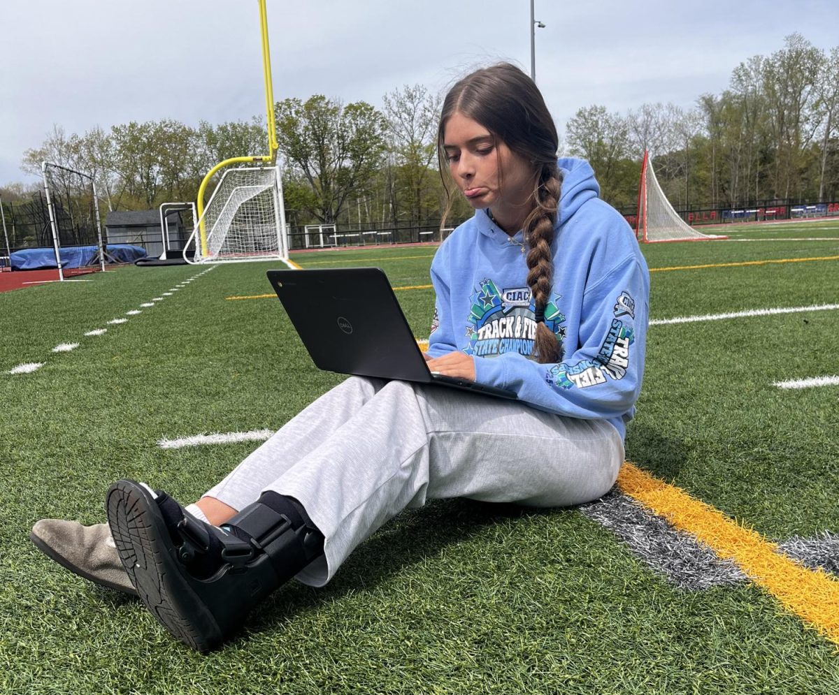 Veronika Nicholas sitting on the football field during practice taking the time to study considering her current status. Balancing athletics, academics, and recovery- the reality behind student life. 