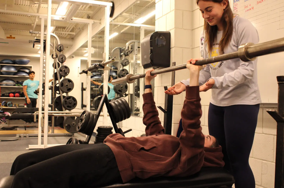 Sophomore Rosie Makarewicz spots sophomore Joceyln McDougall as she bench presses in the Nonnewaug weight room. Many people have found that when the weight room gets crowded, the amount of equipment is insufficient.